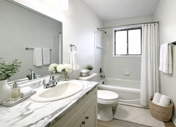 A white bathroom with a marble countertop and a large mirror.