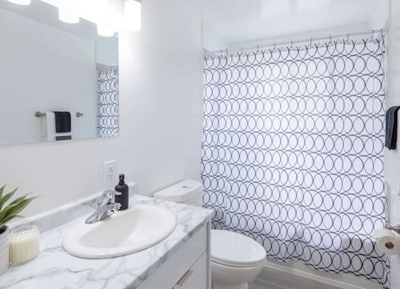 A bathroom with a white sink, toilet, and a shower curtain with a black and white pattern.