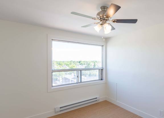 A room with a ceiling fan and a window overlooking a parking lot.