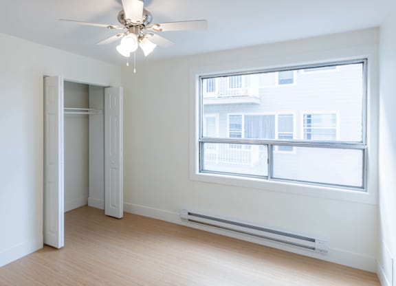 A room with a ceiling fan and a window overlooking a building.