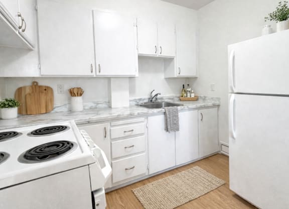 A white kitchen with a stove, sink, and refrigerator.