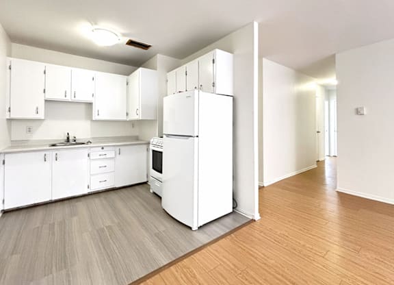 A white kitchen with a white fridge and white cabinets.