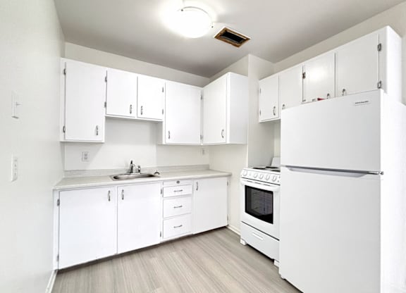 A white kitchen with a refrigerator, sink, and cabinets.