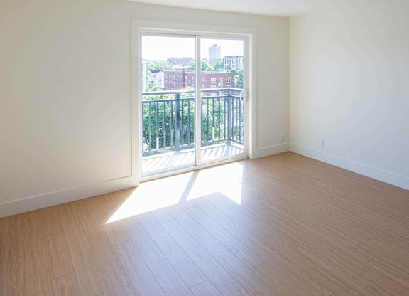 A room with a wooden floor and a view of a city through a sliding glass door.