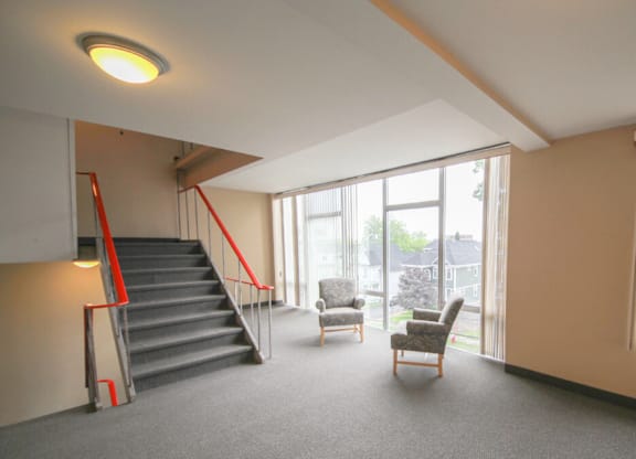 A room with a staircase, chairs, and a window.