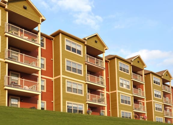 Apartment buildings with balconies and windows are lined up on a grassy hill.