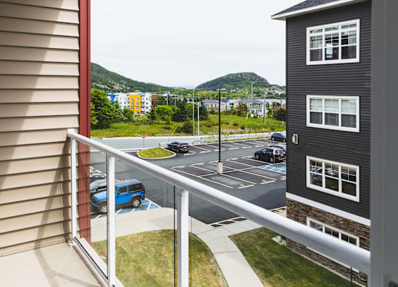 A balcony overlooks a parking lot and a mountain.