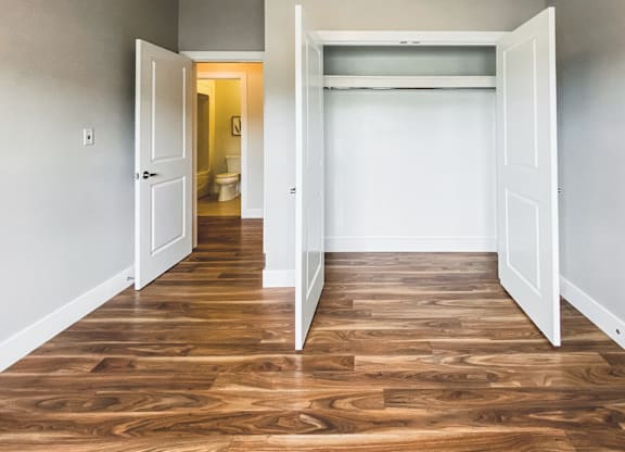 A room with a wooden floor and white walls with two open doors.