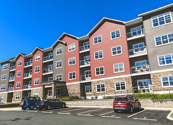 A parking lot in front of a multi-story apartment building with cars parked.