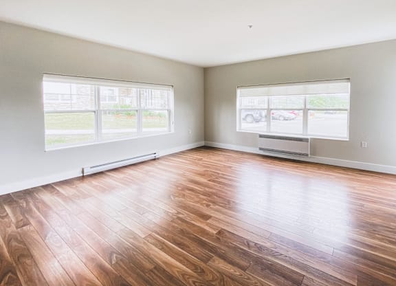 A room with wooden flooring and two windows.