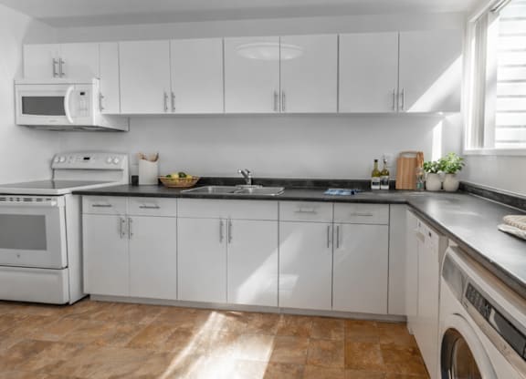 A kitchen with white cabinets and appliances, a tiled backsplash, and a wooden floor.