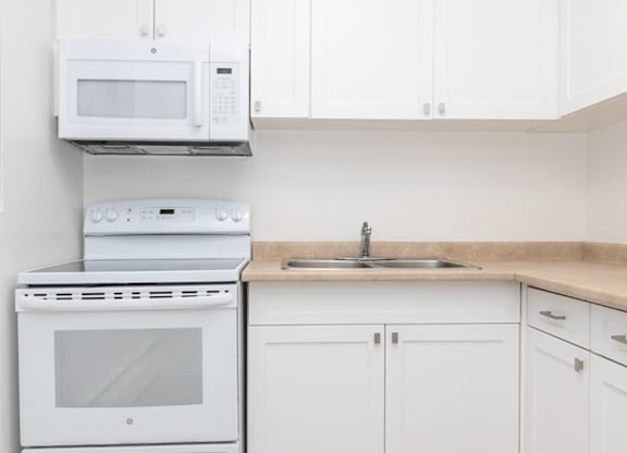 A white kitchen with a stove, oven, microwave, and cabinets.