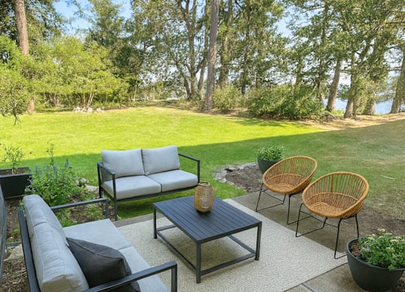 A patio with a black table and chairs with a view of a grassy field and trees.