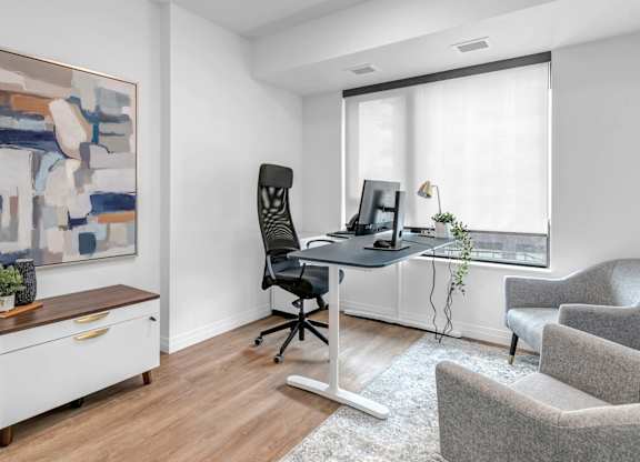 A room with a desk, chair, and a painting on the wall.