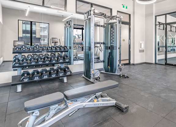 A gym with a variety of equipment including dumbbells, weight plates, and a leg press machine.