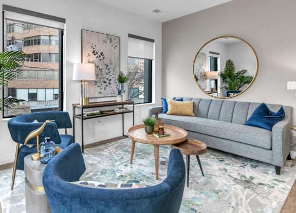 A living room with a grey couch, blue armchair, and a round mirror.