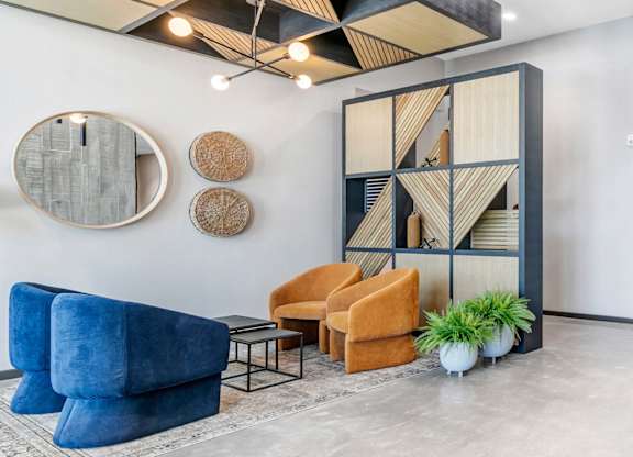 A modern living room with a blue velvet sofa, a wooden shelf, and a round mirror on the wall.