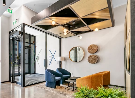 A modern waiting area with a glass door, a blue chair, a brown chair, and a potted plant.