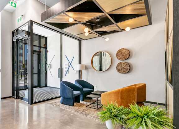 A modern waiting area with a glass door, a blue chair, a brown chair, and a potted plant.