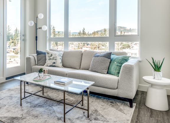 A living room with a grey couch, a glass coffee table, and a large window overlooking a snowy landscape.