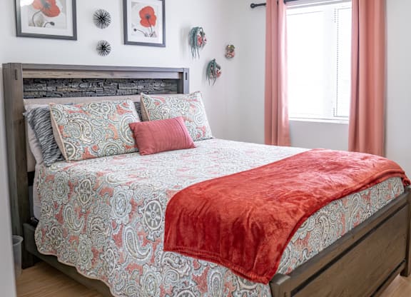 A bed with a red blanket and a grey and red patterned duvet cover.