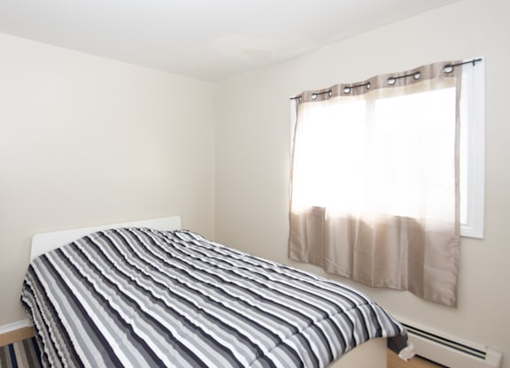 A bed with a striped comforter sits in a room with a window.