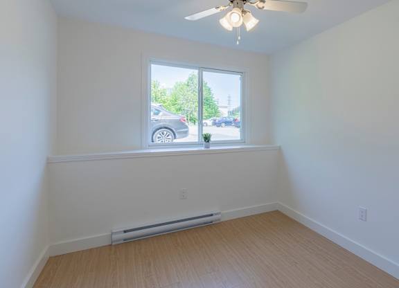 A room with a ceiling fan and a window with a view of the street.