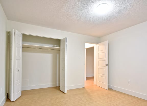 A room with a white wall and a wooden floor with two open doors.