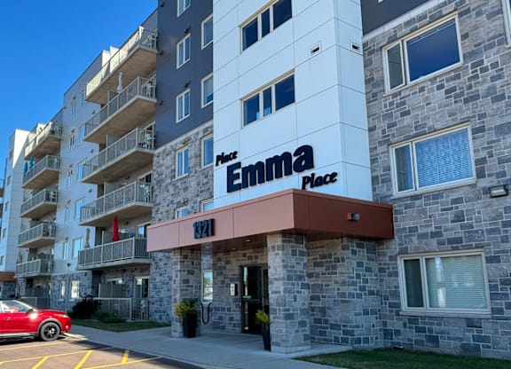 A red car is parked in the parking lot of Emma Place.