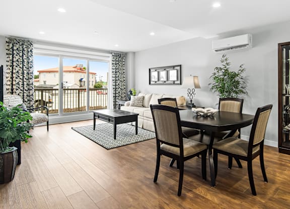 A dining room with a table set for four and a balcony with a view of a house.