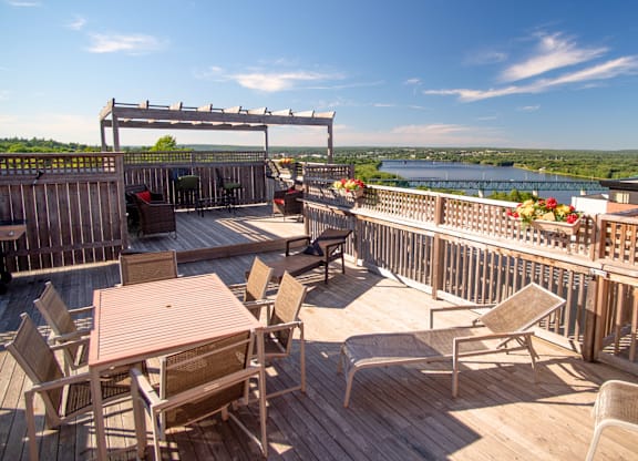 A wooden deck with chairs and a table overlooking a river.