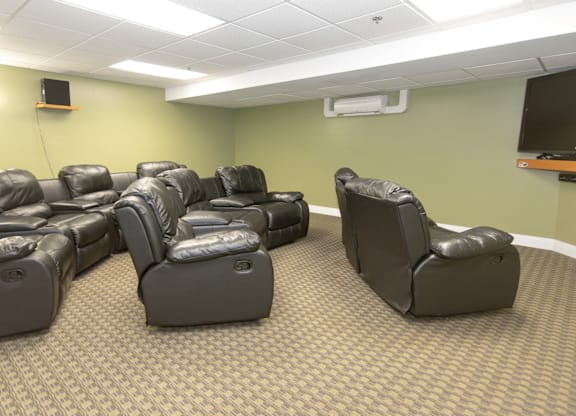 A room with a carpeted floor and rows of black leather recliner chairs.