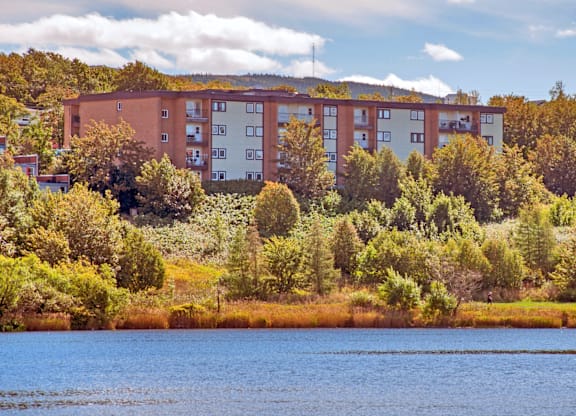 A large building with a red brick exterior is surrounded by trees and bushes.