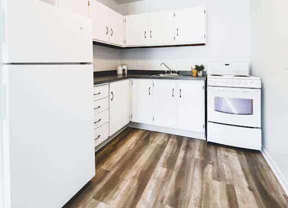 A white kitchen with wood flooring and white appliances.