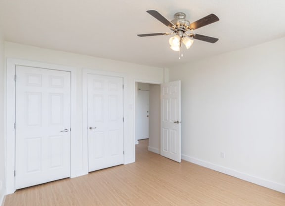 A room with a ceiling fan and three doors.