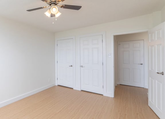 A room with a ceiling fan and three white doors.