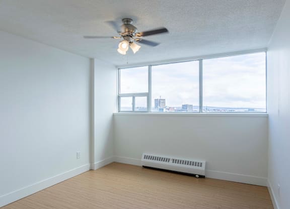 A room with a ceiling fan and a window overlooking a cityscape.