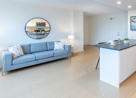 A modern living room with a grey sofa and a round mirror on the wall.