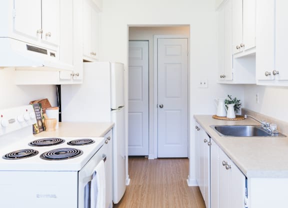 A white kitchen with a stove, sink, and cabinets.