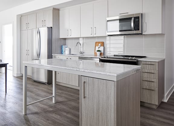 A modern kitchen with a stainless steel refrigerator, microwave, and a marble countertop.