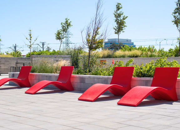 Four red chairs are lined up on a patio.