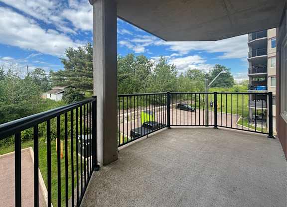 A balcony with a black railing overlooks a green lawn and trees.