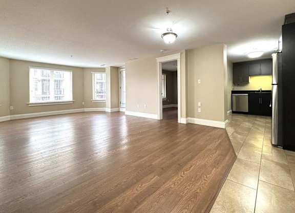 A spacious room with wooden flooring and a black refrigerator.