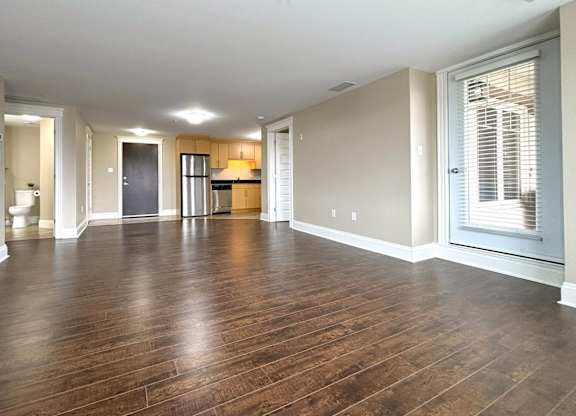 A spacious room with wooden floors and a large window with blinds.