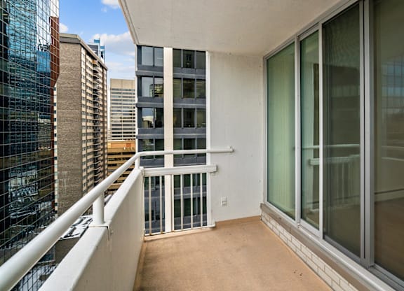 A balcony with a white railing and glass doors overlooks a cityscape.