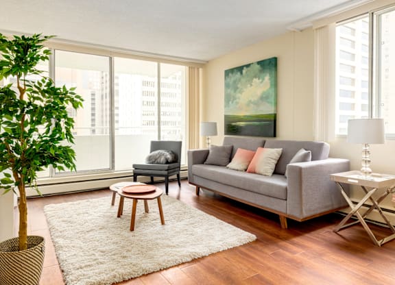 A living room with a grey couch, a wooden coffee table, and a large window with a view of a city skyline.