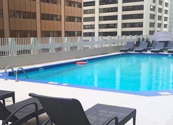 A pool with chairs around it and buildings in the background.