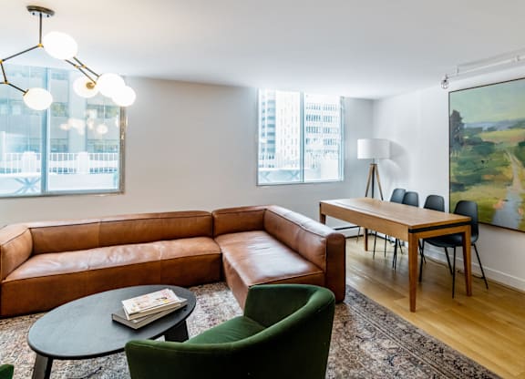 A living room with a brown leather couch, green armchair, and a painting on the wall.