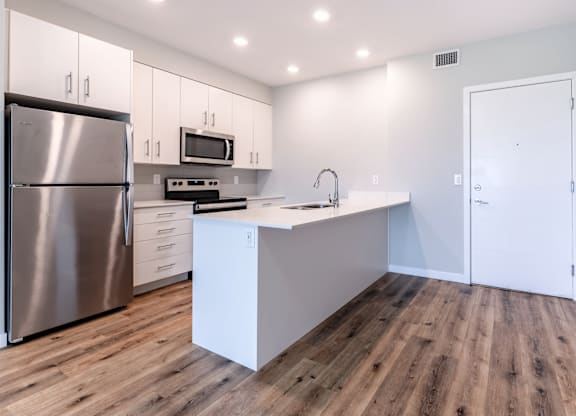 A modern kitchen with a stainless steel refrigerator and wooden flooring.