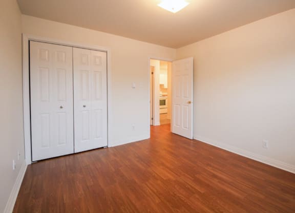 A room with white walls and wooden floors has two white doors.